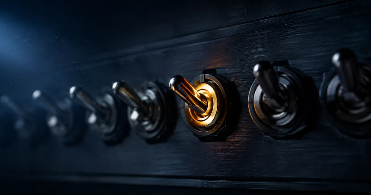 A row of dark industrial toggle switches on a black panel, with a single switch caught mid-flip and glowing amber