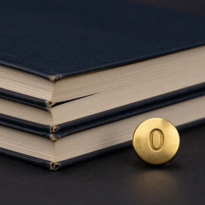 Three bound logbooks stacked beside a round brass transfer button marked 0 on a dark surface